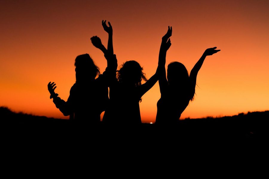 Three girls dance in front of a sunset.