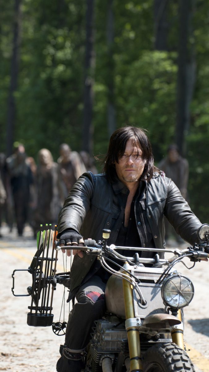 Character, Daryl Dixon, riding a motor cycle away from walkers during The Walking Dead. 