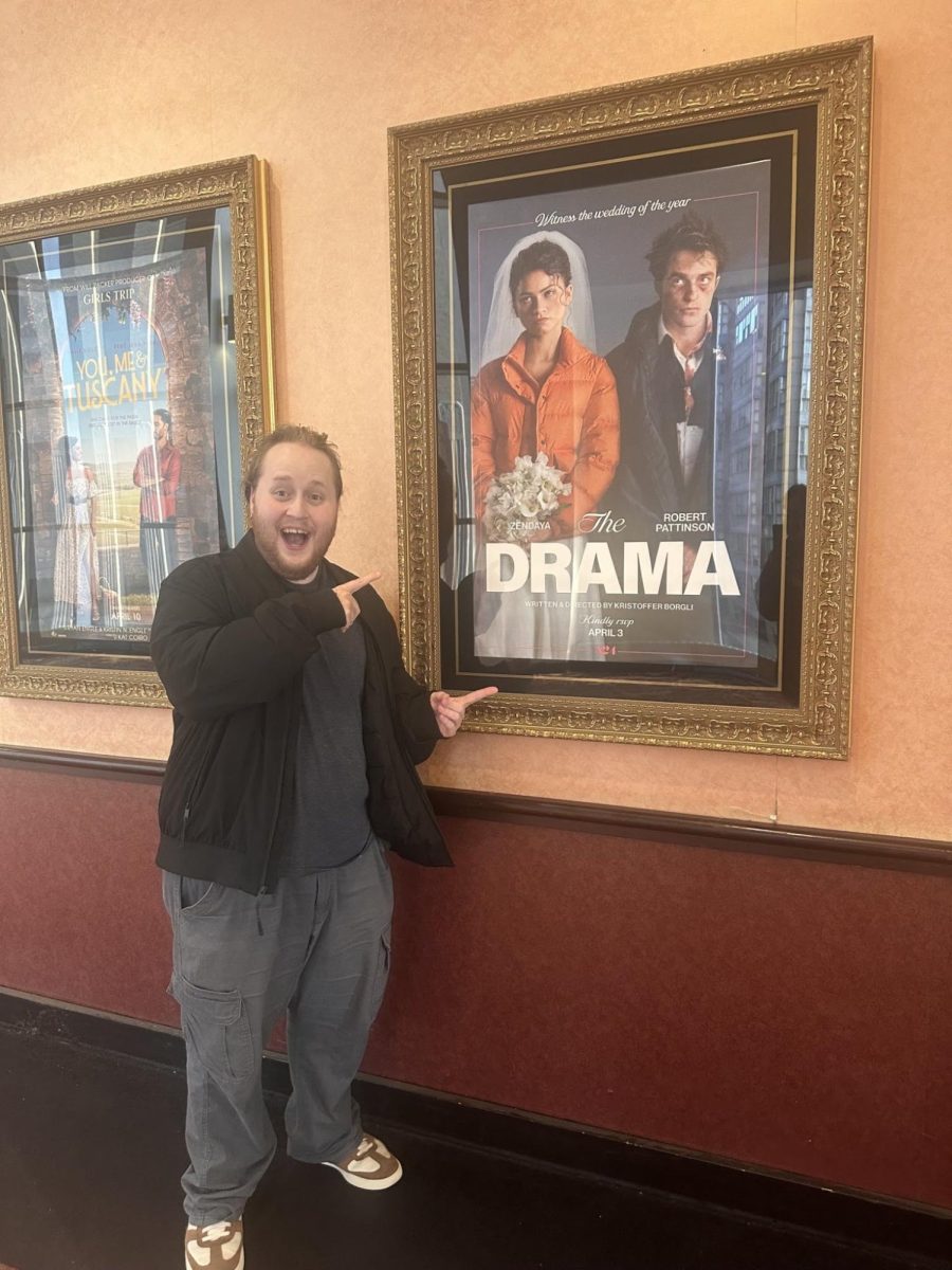 Liam Antwine posing next to a movie poster for 'The Drama.'
